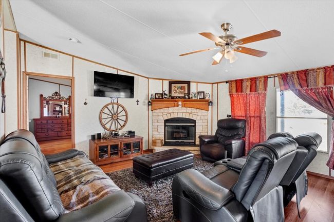 Living room featuring lofted ceiling, a stone fireplace, wood finished floors, visible vents, and a ceiling fan | Image 4