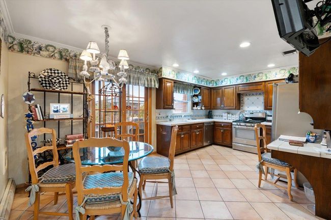 Kitchen featuring an inviting chandelier, crown molding, stainless steel appliances, and light tile patterned flooring | Image 11
