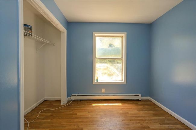 Unfurnished bedroom with a baseboard heating unit, wood finished floors, a closet, and baseboards | Image 8