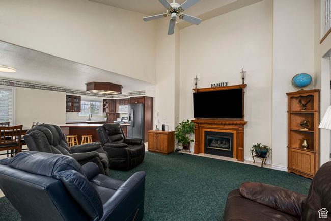 Living area with dark carpet, a ceiling fan, a glass covered fireplace, and a towering ceiling | Image 17