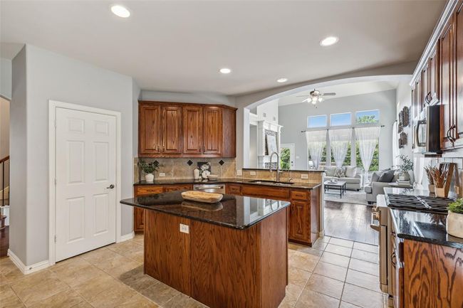 Kitchen with backsplash, ceiling fan, dark stone counters, sink, and a center island | Image 8