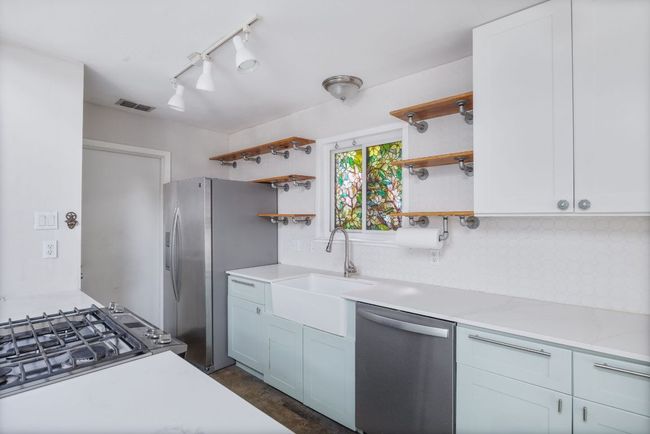 Kitchen featuring stainless steel appliances, open shelves, tasteful backsplash, light stone counters, and rail lighting | Image 7