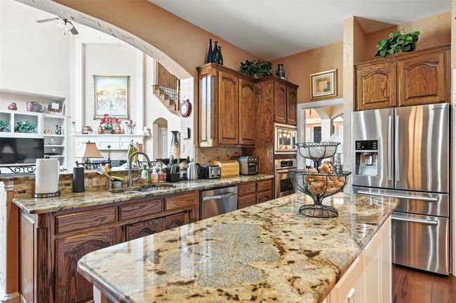 Kitchen with appliances with stainless steel finishes, light stone countertops, a center island, and brown cabinetry | Image 6