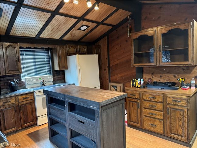 Kitchen featuring light hardwood / wood-style floors, white appliances, butcher block countertops, a kitchen island, and wood walls | Image 9