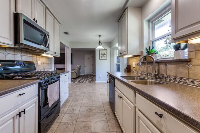 Kitchen featuring black appliances, dark countertops, backsplash, and decorative light fixtures | Image 8