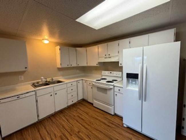 Kitchen with white appliances, under cabinet range hood, dark wood-style floors, light countertops, and white cabinets | Image 9