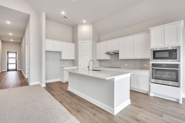 Kitchen with a sink, stainless steel oven, white cabinets, built in microwave, and an island with sink | Image 10