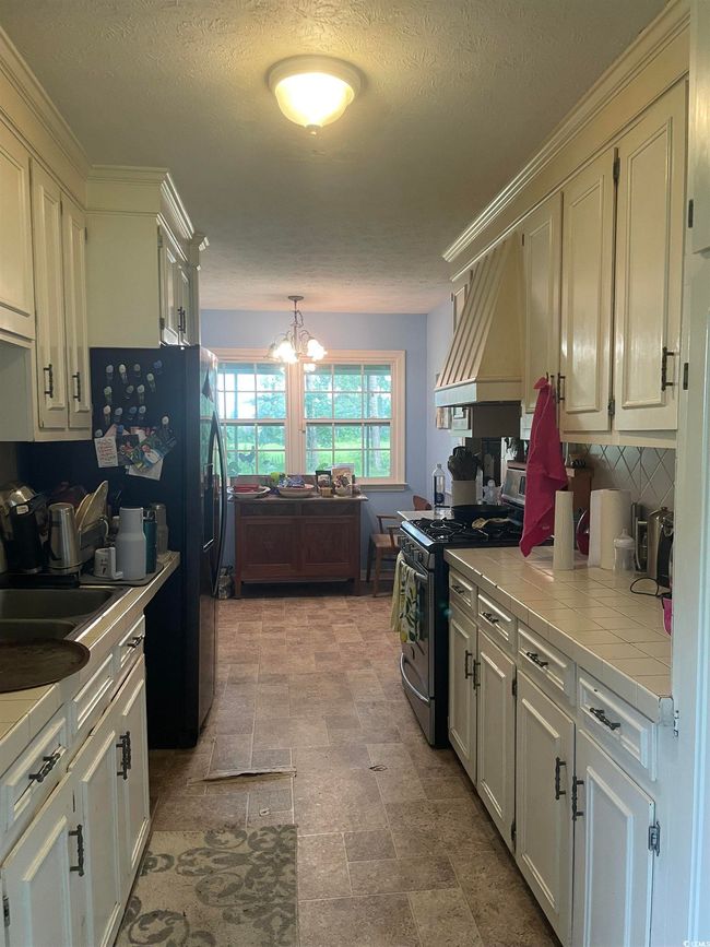 Kitchen featuring gas stove, tile counters, custom range hood, a chandelier, and decorative backsplash | Image 8