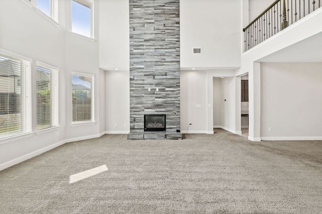 Unfurnished living room with carpet floors, a tile fireplace, baseboards, and a high ceiling | Image 13