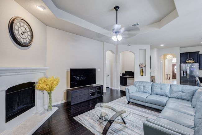 Living area with arched walkways, a raised ceiling, a fireplace, wood finished floors, and baseboards | Image 16