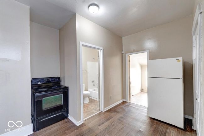 kitchen featuring baseboards, wood finished floors, black / electric stove, and freestanding refrigerator | Image 8