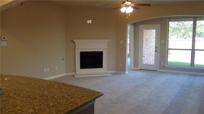Unfurnished living room with ceiling fan, light colored carpet, healthy amount of natural light, and a fireplace with raised hearth | Image 8