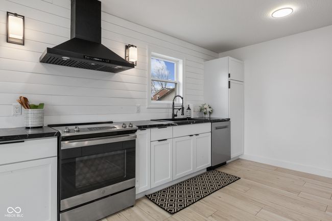kitchen featuring dark countertops, a sink, wall chimney exhaust hood, and stainless steel appliances | Image 30