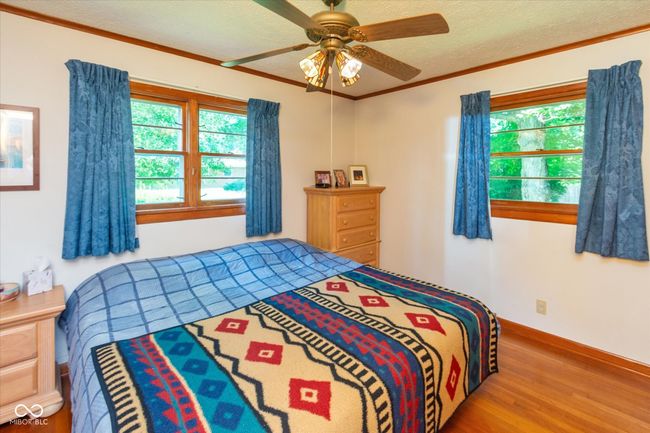 bedroom with wood finished floors, multiple windows, ceiling fan, a textured ceiling, and ornamental molding | Image 15