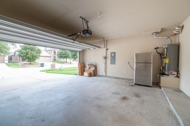 Garage featuring freestanding refrigerator, electric panel, a garage door opener, and electric water heater | Image 31