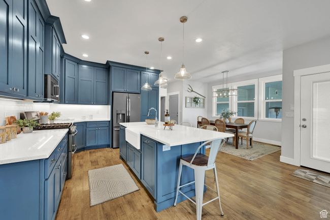 Kitchen with stainless steel appliances, blue cabinets, a breakfast bar, light wood finished floors, and decorative backsplash | Image 13