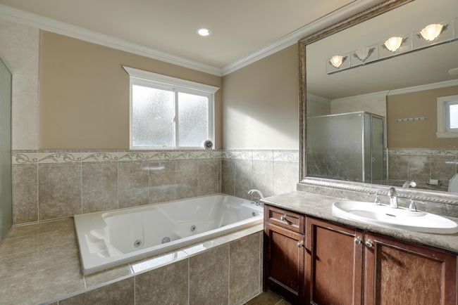 Bathroom featuring a tub with jets, a shower stall, tile walls, ornamental molding, and vanity | Image 24