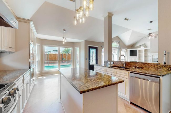 Kitchen featuring dark stone counters, visible vents, a center island, a sink, and stainless steel appliances | Image 14