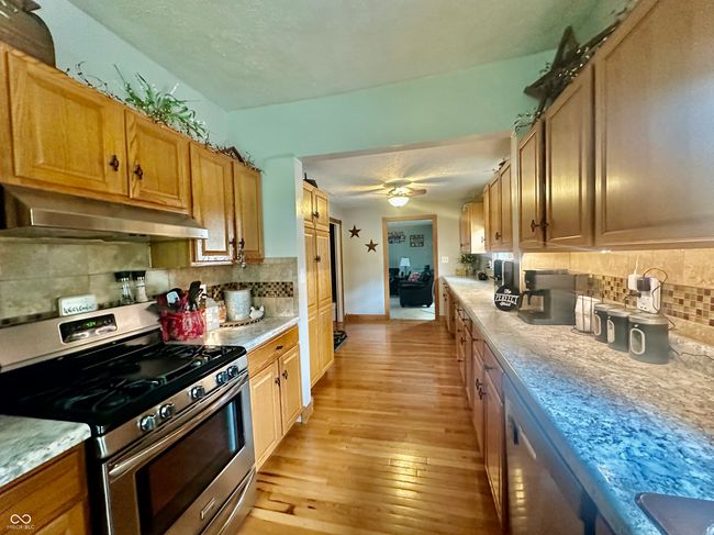 kitchen featuring stainless steel appliances, under cabinet range hood, light wood-style flooring, tasteful backsplash, and light countertops | Image 15