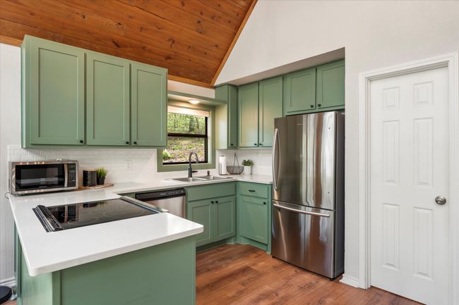 Kitchen featuring green cabinetry, backsplash, a sink, a peninsula, and appliances with stainless steel finishes | Image 23