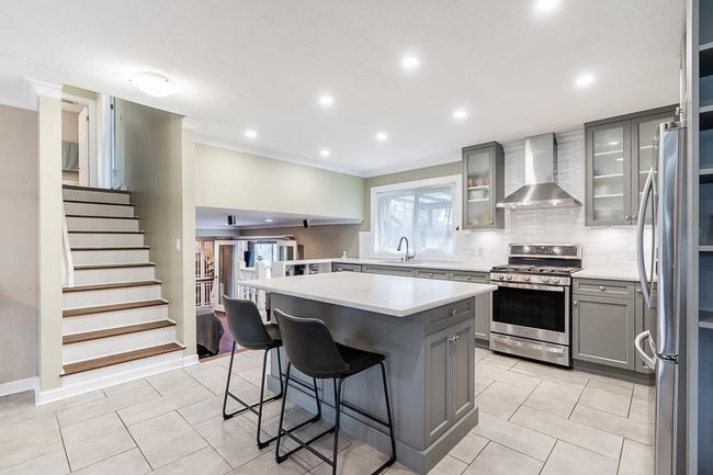 Kitchen with light tile patterned flooring, light countertops, stainless steel appliances, gray cabinetry, and wall chimney range hood | Image 9