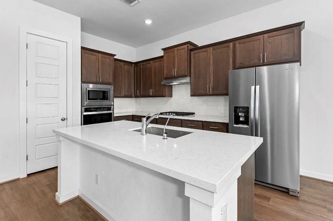 Kitchen featuring stainless steel appliances, a sink, dark brown cabinetry, wood finished floors, and recessed lighting | Image 9