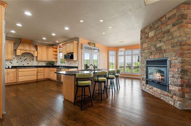 Kitchen with custom exhaust hood, light brown cabinetry, stainless steel appliances, open shelves, and dark countertops | Image 14