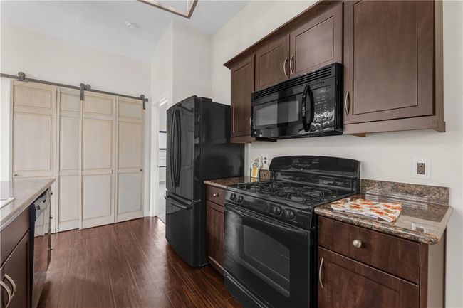Kitchen with black appliances, dark brown cabinetry, dark stone countertops, dark wood-style flooring, and a barn door | Image 9