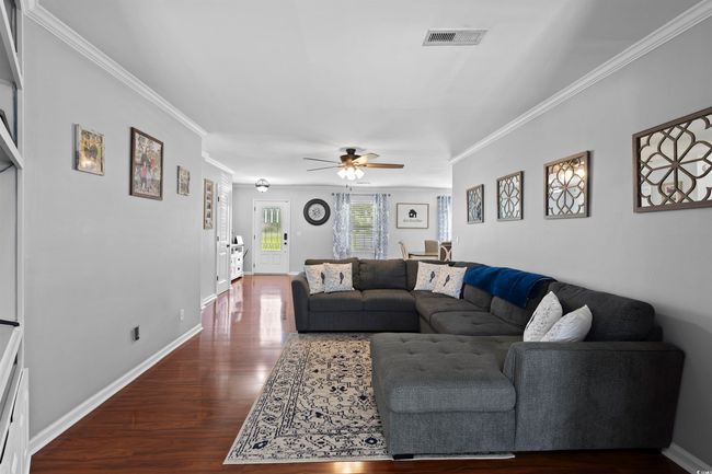 Living room with ceiling fan, dark wood-style flooring, crown molding, and baseboards | Image 7