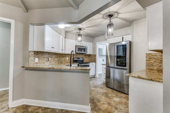 Kitchen featuring appliances with stainless steel finishes, backsplash, light stone counters, white cabinetry, and stone finish floors | Image 10