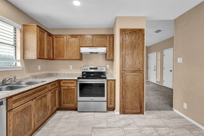 Kitchen with light countertops, visible vents, appliances with stainless steel finishes, under cabinet range hood, and a sink | Image 5