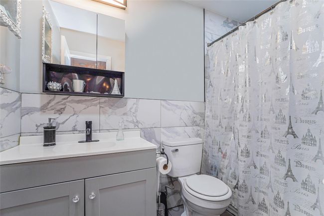 Bathroom with toilet, a shower with shower curtain, tile walls, and vanity | Image 14