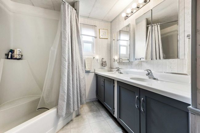Bathroom with double vanity, shower / bath combination with curtain, a sink, and tile patterned floors | Image 21