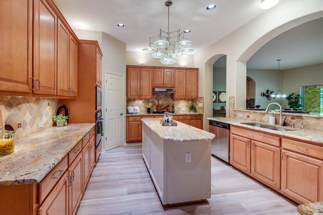 Kitchen with stainless steel appliances, decorative backsplash, a kitchen island, light stone countertops, and light wood-type​​‌​​​​‌​​‌‌​‌‌​​​‌‌​​‌‌​‌​​​​​‌ flooring | Image 18