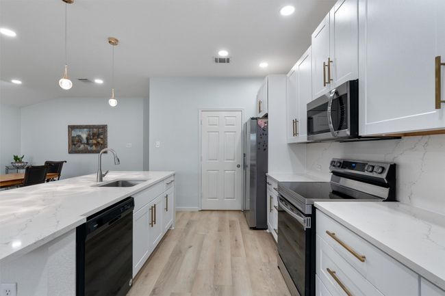 Stainless steel appliances, backsplash, white cabinetry, and decorative light fixtures | Image 12