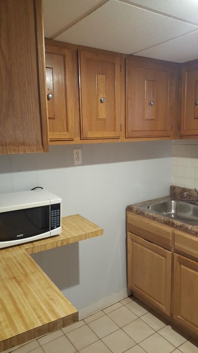 Kitchen with white microwave, butcher block counters, brown cabinets, a sink, and light tile patterned floors | Image 25