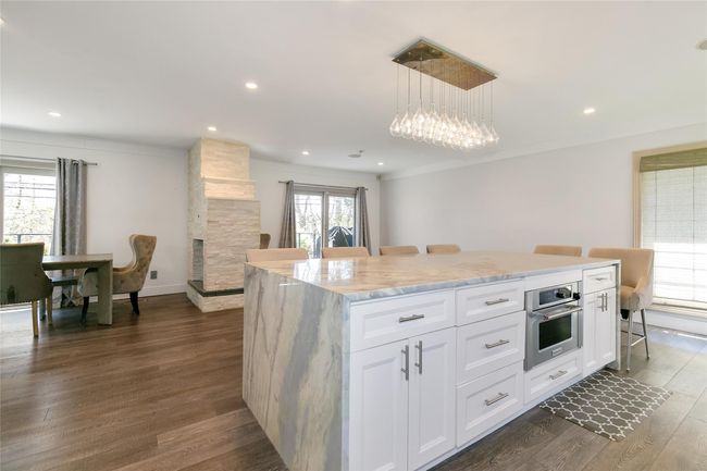 Kitchen with dark wood-style flooring, a fireplace, oven, a center island, and white cabinets | Image 11