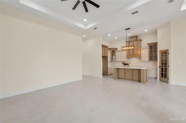 Kitchen featuring recessed lighting, a ceiling fan, light countertops, a kitchen island with sink, and glass insert cabinets | Image 6