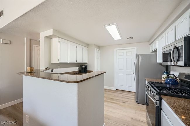 Kitchen with light wood finished floors, stainless steel appliances, a peninsula, baseboards, and white cabinetry | Image 6