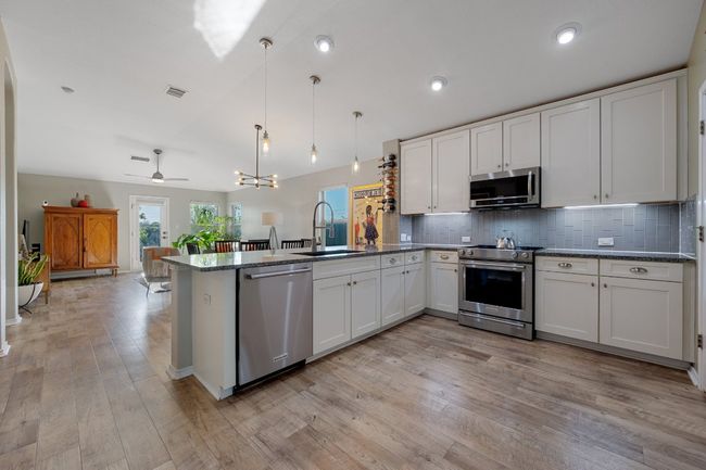Kitchen featuring visible vents, a sink, appliances with stainless steel finishes, a peninsula, and decorative backsplash | Image 4
