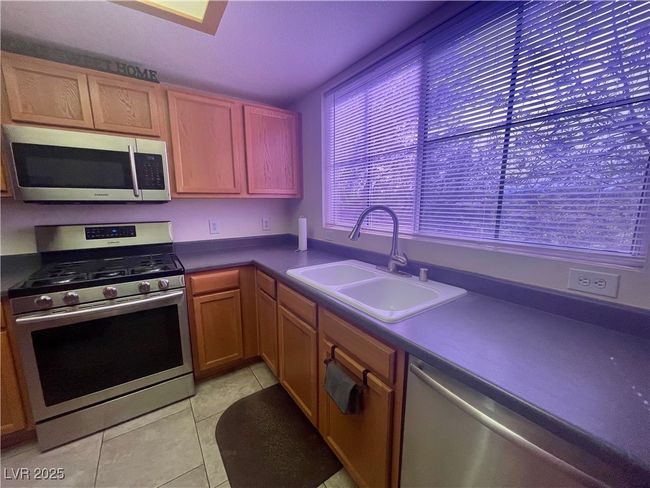 Kitchen featuring dark countertops, light tile patterned floors, a sink, and appliances with stainless steel finishes | Image 11