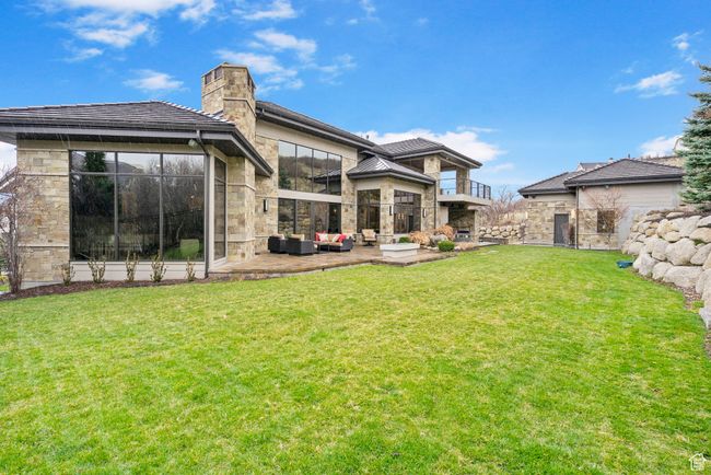 Rear view of house with stone siding, a lawn, a chimney, an outdoor living space, and a patio | Image 94