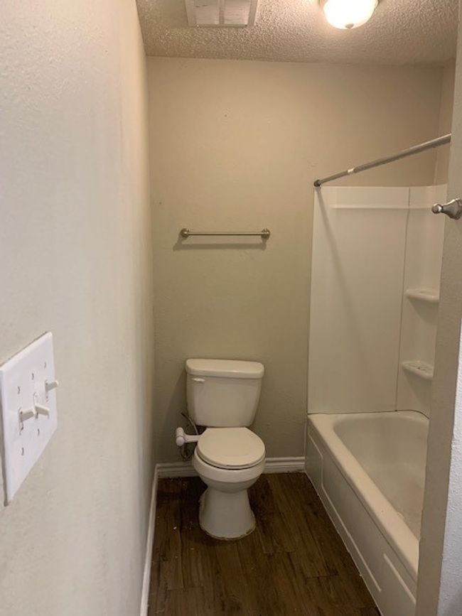 Bathroom with wood finished floors, toilet, a textured ceiling, baseboards, and shower combination | Image 12