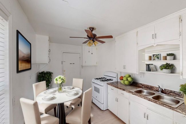 Kitchen with white gas range, open shelves, ceiling fan, and white cabinetry | Image 7
