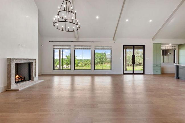 The living room features a distressed stone fireplace surround in a wall that vaults to the ceiling. Around the stone fireplace surround, the walls have been plastered for an extra layer of texture and sheen. Triple windows provide views across the hillside pastures. Adjacent to the wet bar and dining areas, this space is comfortable and casual. | Image 4
