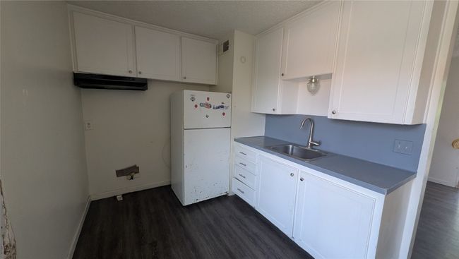 Kitchen with freestanding refrigerator, dark countertops, dark wood-type flooring, white cabinets, and a textured ceiling | Image 6