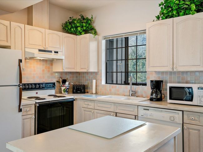 Kitchen featuring white appliances, decorative backsplash, light countertops, under cabinet range hood, and a sink | Image 12