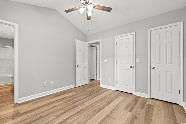 Unfurnished bedroom featuring light wood-style floors, vaulted ceiling, ensuite bath, and a ceiling fan | Image 17