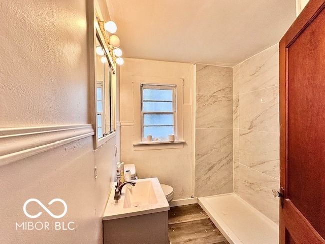 full bathroom featuring a shower, wood finished floors, vanity, toilet, and a textured wall | Image 7