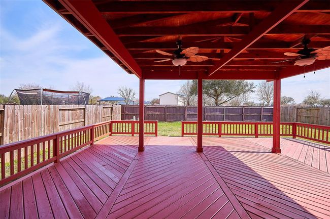 This photo features a spacious, covered outdoor deck with a striking red finish, ceiling fans, and ample railing. It overlooks a fenced backyard, providing a private and inviting space for relaxation or entertainment. | Image 45